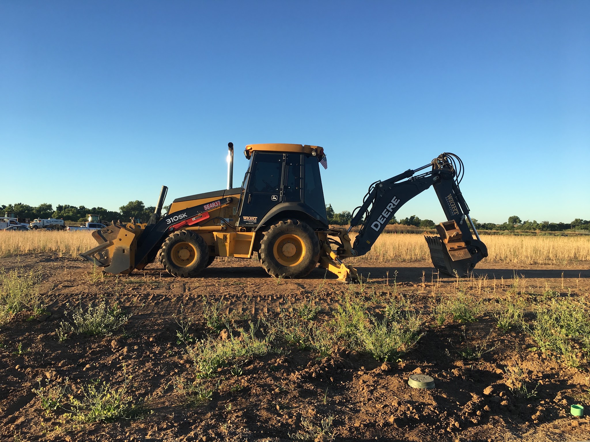 Wight Excavating backhoe with company name painted on the boom, parked in an open field at golden hour