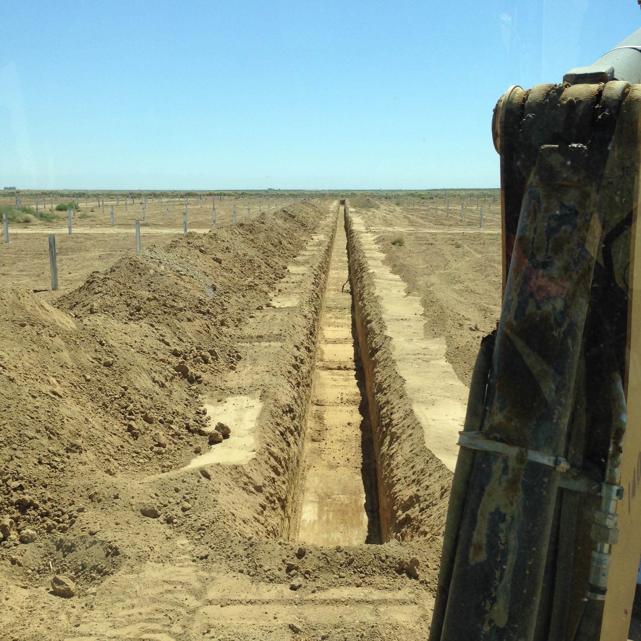 View from the cab down a long freshly dug irrigation trench in an agricultural field