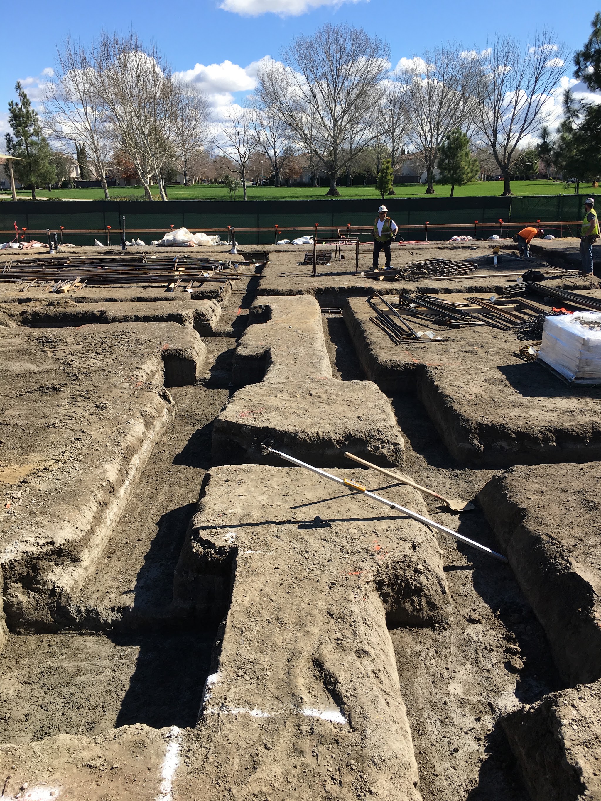 Crew laying rebar on a commercial foundation site with a suburban backdrop